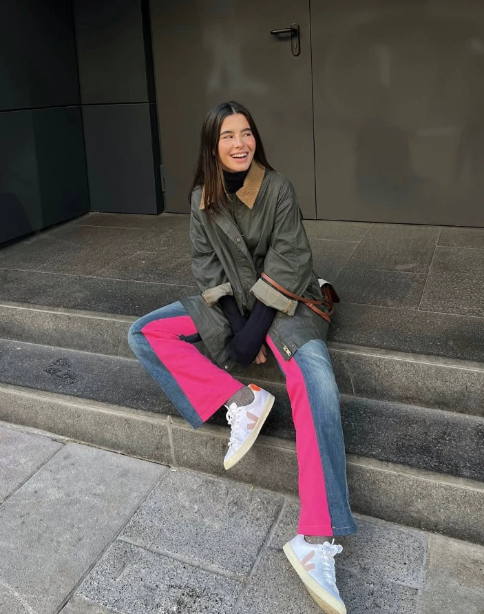 Chica sentada en unas escaleras con vaqueros anchos y paneles laterales en rosa fucsia