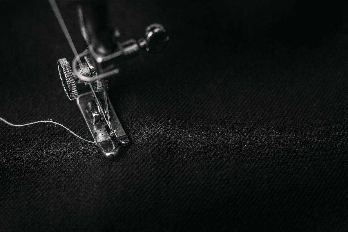 Pie prensatelas de una máquina de coser con hilo sobre una tela negra, en blanco y negro