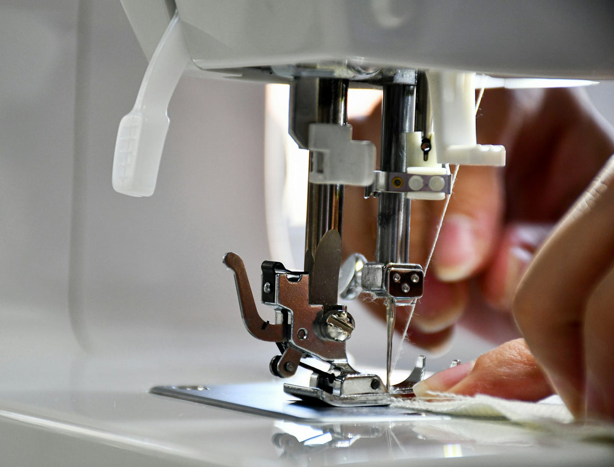 Primer plano de una máquina de coser con los dedos guiando la tela bajo el prensatelas