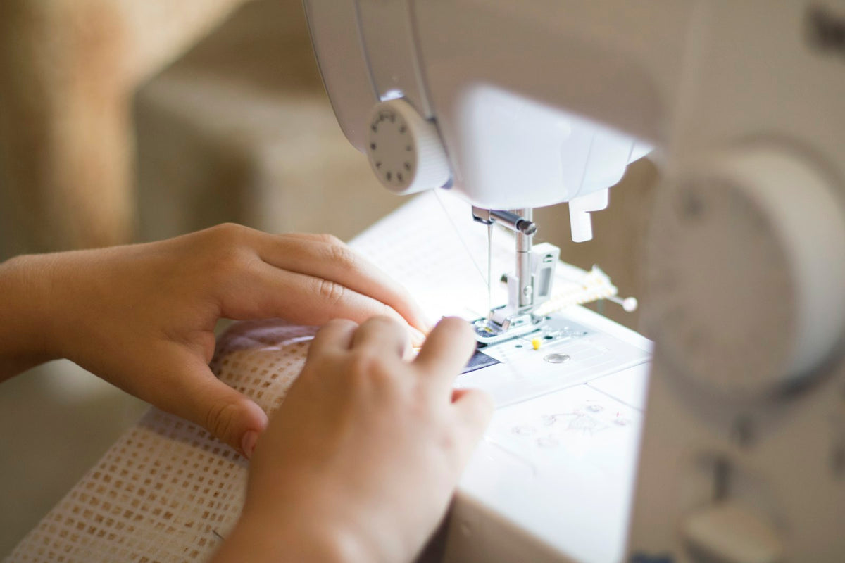 Manos guiando una tela bajo el prensatelas de una máquina de coser